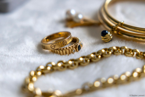 Goldringe, Armbänder und Ketten mit Edelsteinen auf strukturierter Oberfläche
